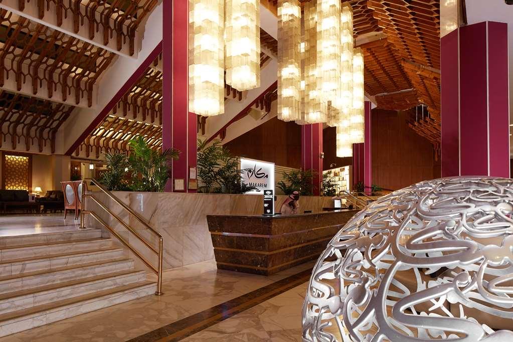 Makarem Ajyad Makkah Hotel Mecca Interior photo The photo depicts a luxurious hotel lobby. It features a grand entrance with a staircase leading up to a reception area. The lobby has high ceilings adorned with striking, modern light fixtures that hang down, providing a warm ambiance. The walls are