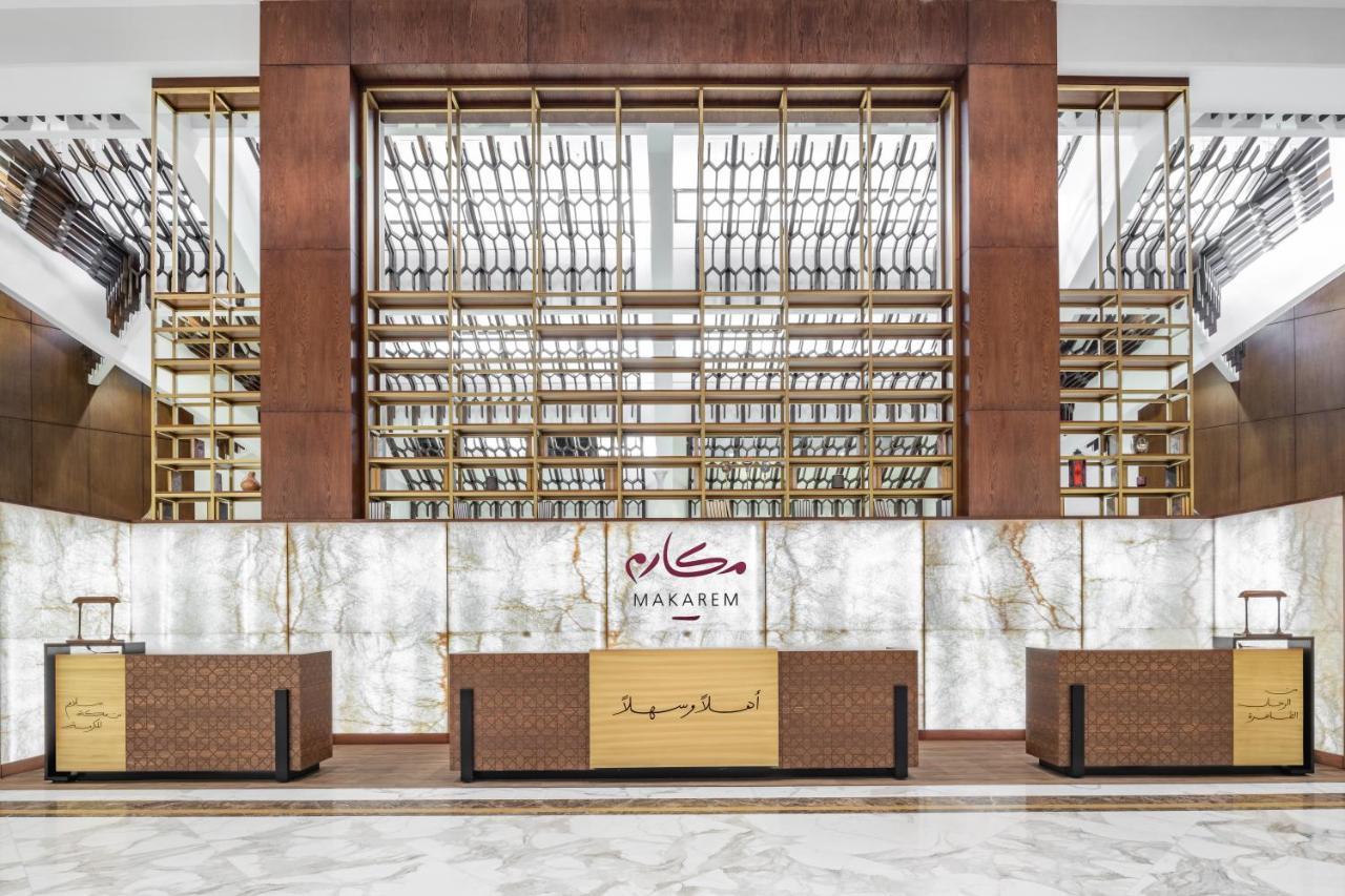 Makarem Ajyad Makkah Hotel Mecca Exterior photo The photo shows the interior of a hotel or a reception area, characterized by a modern and elegant design. In the foreground, there are multiple reception desks with a polished finish. Behind the desks, a striking feature is a wooden wall with a geom