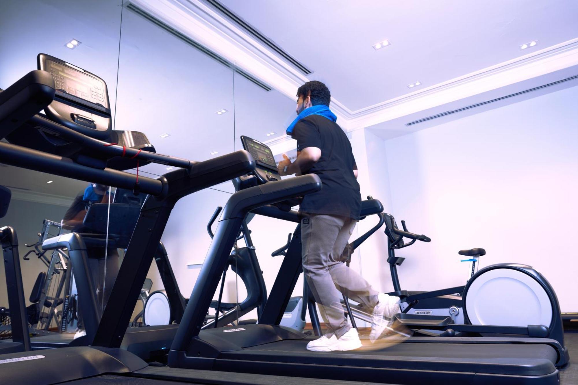 Makarem Ajyad Makkah Hotel Mecca Exterior photo The photo shows a person exercising on a treadmill in a modern gym or fitness room. The individual is wearing a blue neck support while jogging on the treadmill, which is set against a backdrop of large mirrors. There are also additional exercise equ