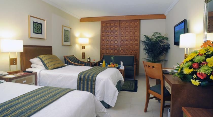 Makarem Ajyad Makkah Hotel Mecca Exterior photo The photo shows a hotel room featuring two single beds with white linens and green and blue striped throw blankets. There is a wooden headboard behind the beds and a decorative wooden partition or wall in the background. A cozy seating area is visibl