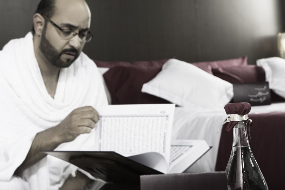 Makarem Ajyad Makkah Hotel Mecca Exterior photo The photo shows a man engaged in reading a book or document, seated in a room with a relaxed atmosphere. He is wearing traditional white attire, often associated with specific cultural or religious practices. In the foreground, there is a bottle, pos